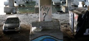 One of the pillars under the bridge at Julia Tuttle Causeway. On the left, a car. On the right, a hut made from metal and plastic sheets. On the pillar someone wrote "Why?" with black spray paint.
